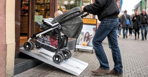 Hürdenlos rein mit der mobilen Rampe (Foto: Tobias Dittmer) Ein Mann schiebt ein Kind im Kinderwagen über eine Rampe in ein Ladengeschäft