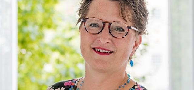 Eine mittelalte Frau mit Brille lächelt in die Kamera.