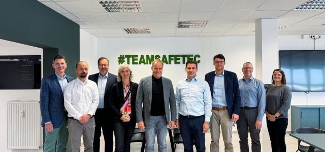 Eine Gruppe von Personen hat sich zum Gruppenbild aufgestellt. An der Wand hinter ihnen steht "#TeamSafetec".