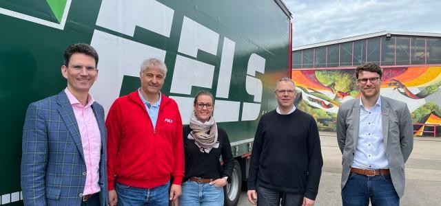 Vier Männer und eine Frau stehen vor einem LKW und schauen in die Kamera.