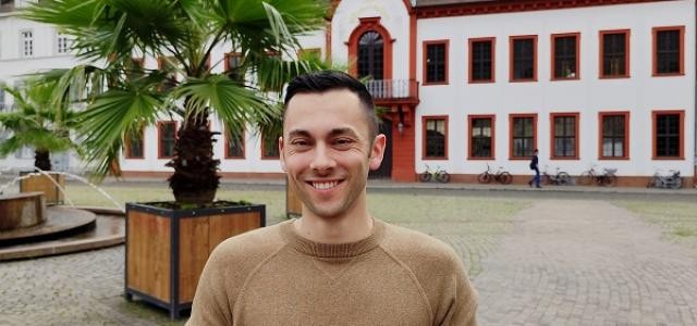 Luckas Nickus steht auf dem Karlsplatz und hält Flyer in den Händen. Im Hintergrund das Schloss.