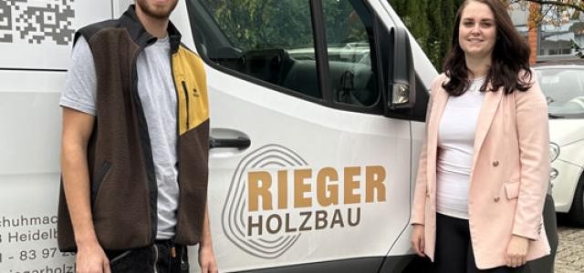 Ein Mann und eine Frau stehen vor einem Handwerkerfahrzeug und schauen in die Kamera.