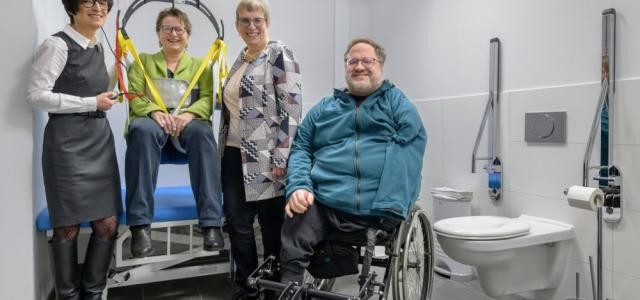 Eine höhenverstellbaren Pflegeliege mit Lifter für Erwachsene gehört zur Ausstattung der „Toilette für alle“. Das Foto zeigt von links beim Test des Lifters: Bürgermeisterin Stefanie Jansen, die Behindertenbeauftragte der Stadt Heidelberg Christina Reiß, die Geschäftsführerin des Landesverbands der Körper- und Mehrfachbehinderten (LVKM) Jutta Pagel-Steidl sowie den Vorsitzenden des Beirats von Menschen mit Behinderungen Czeslaus Mandalka.
