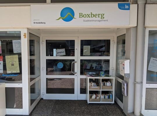 Heidelbergs erstes Wasserquartier wurde unter der Federführung des Stadtteilmanagements Boxberg gegründet. Seit Mai gab es verschiedene Aktionen rund um das Thema Wasser und Nachhaltigkeit. Kostenloses Leitungswasser gibt es bei den fünf Refill-Stationen, z.B. im Büro des Stadtteilmanagements Boxberg. (Foto: Judith Schwarz) Blick auf eine Glastür mit einem kleinen Bücherregal davor.