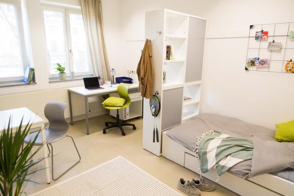 So oder ähnlich könnte ein Zimmer im Fachkräftehaus in Heidelberg aussehen. (Foto: Bormann) Blick in ein Zimmer mit Schreibtisch, Trennregal, Tisch und Bett.