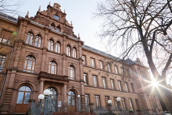 Die neuen Fenster des Kurfürst-Friedrich-Gymnasiums erfüllen moderne Schallschutzanforderungen und behalten eine historisch korrekte Optik. (Foto: Stadt Heidelberg) Die Sonne erstrahlt ein großes Sandsteingebäude.