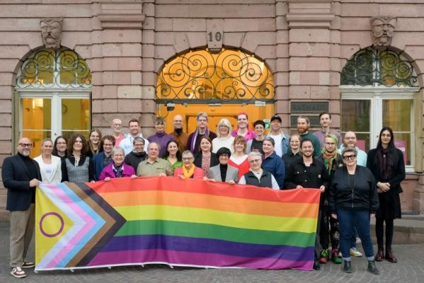 Engagiert für die Rechte und Sichtbarkeit von queeren Menschen: Mitglieder des „Runden Tischs sexuelle und geschlechtliche Vielfalt“ mit der Progress Pride Flagge vor dem Heidelberger Rathaus. (Foto: Rothe) Gruppenfoto mit einer Progress Pride Flagge.