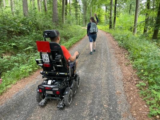 Mit dem geländetauglichen Elektrorollstuhl auf Tour im Heidelberger Stadtwald. (Foto: Claudia Hanko) Mann fährt mit E-Rolli auf einem Waldweg mit einer Begleitung, die vorausgeht.