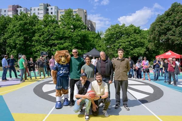 Freude über den neugestalteten Basketballplatz auf dem Emmertsgrund – stehend von links: „Accy“, Maskottchen der MLP Academics Heidelberg, Künstler Florian Budke, Nina Schandorf, 1. Vorsitzende des Vereins Hip Hop Heidelberg, Oberbürgermeister Eckart Würzner sowie Michael Steinke, Vorsitzender des Jugendgemeinderats; kniend von links: die Stadträte Bülent Teztiker und Felix Grädler. (Foto: Rothe) Sieben Personen, inklusive eines Maskottchen in einem Äffchenkostüm, posieren auf einem Basketballplatz und halten einen Basketball, im Hintergrund, buntes Treiben.