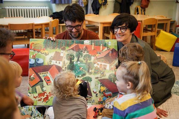 Bürgermeisterin Stefanie Jansen besuchte die neue queere Familiengruppe in der Plöck 2a. (Foto: Stadt Heidelberg) Eine Frau und ein Mann zeigen kleinen Kindern ein großes Bilderbuch.