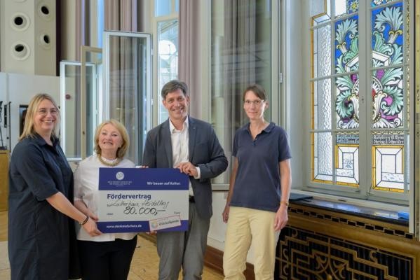 Erster Bürgermeister Jürgen Odszuck (2. v. r.) besichtigt bei seiner Baustellen-Sommertour die Arbeiten zur Fenstersanierung an der Musik- und Singschule. Dabei kann er eine Förderung über 80.000 Euro von der Deutschen Stiftung Denkmalschutz entgegennehmen, die Ortskuratorin Helen Heberer (2. v. l.) übergibt. (Foto: Philipp Rothe) Erster Bürgermeister Jürgen Odszuck nimmt vor der Fensterfront den großen Scheck von Helen Heberer entgegen.