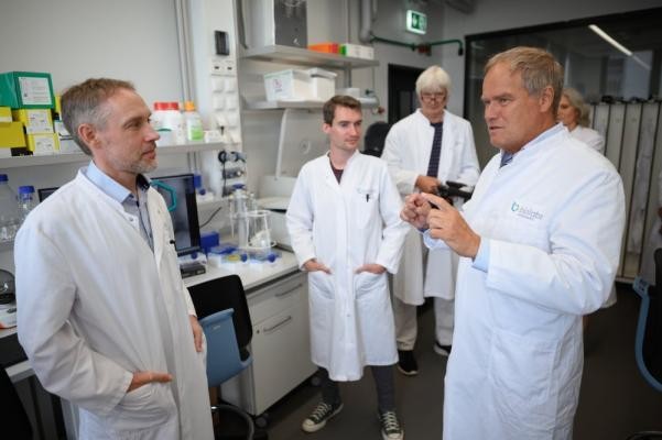 Dr. Markus Krohn (l.), einer der Geschäftsführer des Start-ups Bimovis, erläuterte Oberbürgermeister Eckart Würzner (r.) die Ziele und Tätigkeiten des Unternehmens. (Foto: Stadt Heidelberg) Oberbürgermeister Eckart Würzner steht mit Dr. Markus Krohn und 3 weiteren Labortmitarbeitenden im Labor.  Alle tragen weiße Laborkittel.