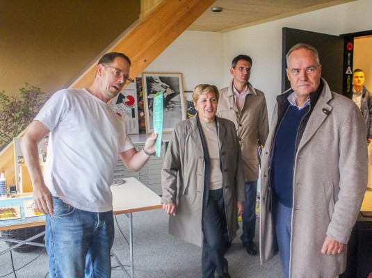 Götz Gramlich (links), Gesellschafter von Tdrei, zeigte Ministerin Nicole Razavi, Oberbürgermeister Eckart Würzner (rechts) und Marc Massoth, Leiter des Amts für Wirtschaftsförderung und Wissenschaft, die Somerville-Arkaden in den ehemaligen Stallungen. Ein Mann führt eine Gruppe Besucher durch ein ehemaliges Stallgebäude.