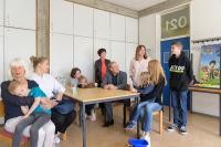 Oberbürgermeister Prof. Dr. Eckart Würzner und Sozialbürgermeisterin Stefanie Jansen (Mitte stehend) besuchten zum offiziellen Start am 30. Mai die Begegnungsstätte für ukrainische Geflüchtete in der ehemaligen Julius-Springer-Schule auf dem Schulcampus in der Südstadt. Natalia Jäger (3.v.l.) ist dort die verantwortliche Ansprechpartnerin. (Foto: Rothe) Foto mit Erwachsenen und Kindern am Tisch