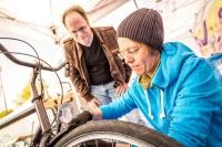 Kleinere Wartungsarbeiten wie Bremsen nachstellen, Reifen aufpumpen oder Kette ölen werden beim RadCheck sofort erledigt. (Foto: Initiative RadKULTUR, Ministerium für Verkehr Baden-Württemberg, Heiko Simayer) Eine Person arbeitet an einem Fahrrad, während eine weitere Person ihr über die Schulter schaut