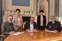 Leitender Staatsanwalt Andreas Herrgen, Oberbürgermeister Prof. Dr. Eckart Würznerund Polizeipräsident Siegfried Kollmar unterzeichnen den „Letter of Intent“ zur Einrichtung eines Hauses des Jugendrechts in Heidelberg, dahinter die Ministerin der Justizund für Migration Baden-Württemberg, Marion Gentges MdL, und Bürgermeisterin Stefanie Jansen (Dezernentin für Soziales, Bildung, Familie und Chancengleichheit derStadt Heidelberg). (Foto: Peter Dorn) drei Perosnen sitzen gemeinsam an einem Tisch und unterschreiben auf einem Papier, welches vor ihnen liegt.
