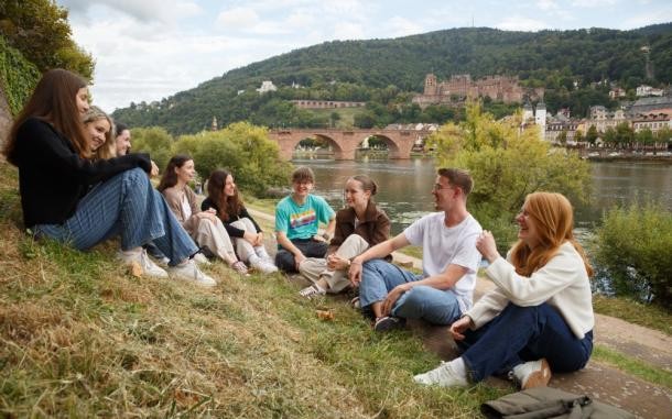 Mitreden in Heidelberg: Junge Menschen im Alter zwischen 13 und 19 Jahren haben ab 25. September die Möglichkeit, für den Jugendgemeinderat zu kandidieren. (Foto: Stadt Heidelberg) Neun Jugendliche sitzen in einem Halbkreis zusammen am Neckar.