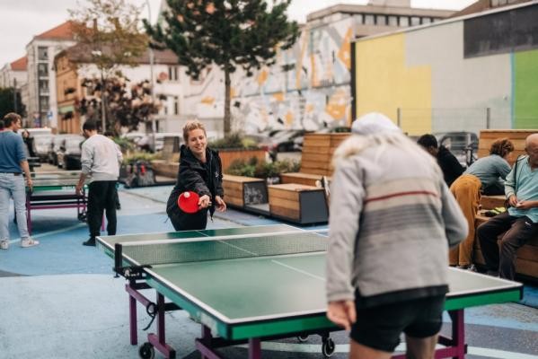 Wo früher Autos parkten, wird heute gespielt: Der Ping-Pong-Social-Club brachte mit seinen Tischtennis-Aktionen Bewegung in den Emil-Maier-Park.(Foto: Niko da Silva Neithardt) Zu sehen sind eine junge Frau und ein älterer Herr die unter freiem Himmel Tischtennis auf einer grünen Tischtennisplatte spielen. Hinter ihnen spielt noch eine andere Gruppe.