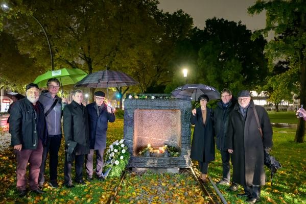 Beim Gedenken an die Opfer von Gurs am Mahnmal in der Schwanenteichanlage (von links): Helmut Haas (Schatzmeister GCJZ Heidelberg), Pfarrer Mirko Diepen (evangelischer Vorsitzender der GCJZ Heidelberg), Michael Schwarzmann (jüdischer Vorsitzender der GCJZ Heidelberg), Rabbiner Janusz E. Pawelczyk-Kissin (Hochschule für jüdische Studien Heidelberg), Bürgermeisterin Stefanie Jansen, Dr. Christof Ellsiepen (Dekan der Evangelischen Kirche Heidelberg), Prof. Dr. Michael Schmitt (Katholischer Vorsitzender der GCJZ Heidelberg). (Foto: Philipp Rothe) 7 in schwarz gekleidete Menschen stehen jeweils rechts und links neben dem Mahnmal