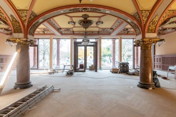 Die Sanierung der Stadthalle befindet sich auf der Zielgeraden – wie auch der Blick in den Meriansaal zeigt. (Foto: Christian Buck) Das Foto zeigt das innere der Stadthalle. Die Decke ist von verzierten Bögen gekennzeichnet und auf dem Boden befinden sich auf dem Parkett noch Bauutensilien, darunter eine Leiter
