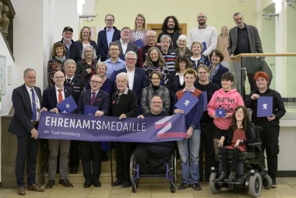 Oberbürgermeister Eckart Würzner (vorne links) verlieh im Rathaus 29 Ehrenamtsmedaillen für außerordentliches Bürgerschaftliches Engagement an: 1. Reihe von links: Jürgen Wiesbeck, Jona Pawelczyk-Kissin, Fritz Zernick, Dr. Christina Reinl, Czeslaus Mandalka (vorne), Konrad Schick, Adrian de Boer (beide Schülis gegen Rechts), Jen Bihr, Heike Stahlmecke (vorne), Leander Großmann (Schülis gegen Rechts). 2. Reihe von links: Martin Krauter, Gudrun Decker, Thomas Frank, Erica Dutzi, Heike Hauck, Ursula Rittmüller. 3. Reihe von links: Prof. Dr. Ute Straub, Gabriele Schneidmüller, Jannik Pohlmann. 4. Reihe von links: Wilfried Münster, Barbara Pfeiffer, Kai Neureuther, Andreas Horsch, Hartmut Tiede, Jutta Schettler, Beverley Mühlbauer. 5. Reihe von links: Wolfgang Rein, Christina Franz (Tochter von Hans Werner Franz, der nicht anwesend war), Abdullah Alahmad, Daniel Ryklin, Wolfgang Graf. Nicht anwesend waren: Uwe Häfner, Christoph Sambel. (Foto: Philipp Rothe) Auf den Stufen im Rathausfoyer stehen die Ausgezeichneten und halten einen Banner.