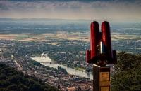 Wirtschaft und Wissenschaft im Blick. (Foto: Schwerdt/Heidelberg Marketing GmbH) Im Vordergrund ein rotes Fernglas, im Hintergrund Heidelberg und der Neckar von oben.