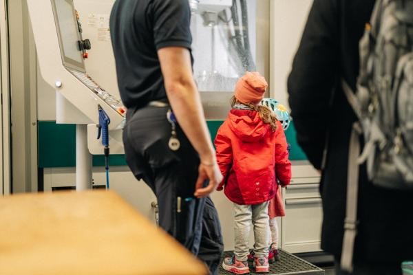 Schon für die Kleinsten gab es bei "explore us" Spannendes zu sehen. (Foto: Oliver Matlok) Zwei Kinder stehen vor einer Maschine und schauen neugierig hinein. Sie sind von hinten fotografiert.