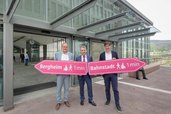 Oberbürgermeister Eckart Würzner (l.), Erster Bürgermeister Jürgen Odszuck (r.) und Kai M. Dreesbeimdiek, Geschäftsführer der Gustav Zech Stiftung Management GmbH, eröffnen die neue Fußgängerbrücke zwischen Hauptbahnhof und Europaplatz. (Foto: Philipp Rothe) Drei Männer stehen vor einer Glastür. Sie halten zwei Schilder in Pfeilform in den Händen.