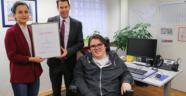 Auszeichnung: Heidelberg unterstützt Menschen mit Behinderung am Arbeits-Platz (Foto: Stadt Heidelberg) Eine Frau und ein Mann halten eine Urkunde hoch. Neben ihnen ist ein junger Mann im Rollstuhl. (Foto: Stadt Heidelberg)