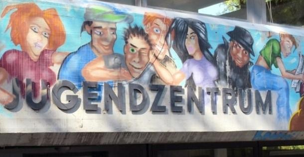 Schriftzug "Jugendzentrum" auf Mauer mit gemalten jungen Menschen