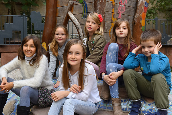 Kindergruppe sitzt vor Haus