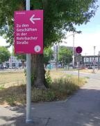 Auf einem heidelbeerfarbenen Schild steht "Zu den Geschäften in der Rohrbacher Straße.