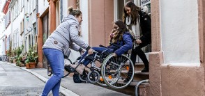 Zwei Frauen tragen eine Frau im Rollstuhl eine Treppe runter (Foto: Pellner)
