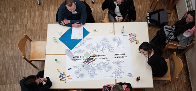 Menschen sitzen an einem Tisch und arbeiten gemeinsam an einem Plakat